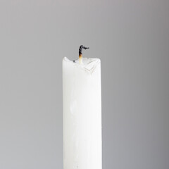 White, burned out candle in front of a grey background