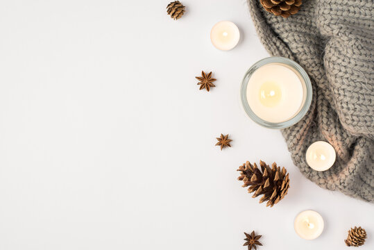 Top view photo of lighted candles grey knitted scarf pine cones and anise on isolated white background with copyspace