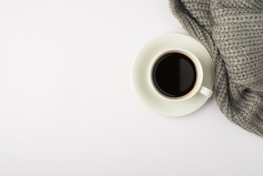 Top view photo of cup of coffee on saucer and grey knitted scarf on isolated white background with copyspace