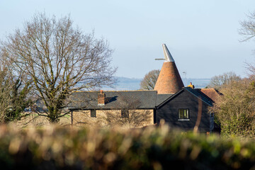 A Kentish oast house with hills (North Downs) visible on the horizon surrounded by trees and framed...