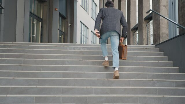 Close up shot of hurry Asian young businessman running up on stair going to work in office. The working man holding business handbag with office formal suit walking outdoor in urban city.