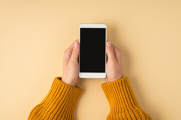 First person top view photo of female hands in yellow sweater holding white smartphone on isolated...