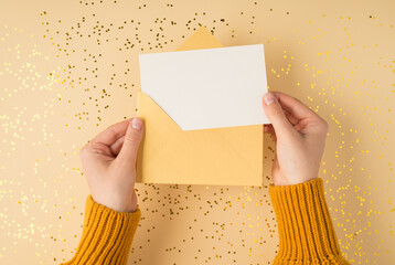 First person top view photo of female hands in yellow pullover holding open pastel yellow envelope...