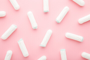 Many new white sanitary tampons on light pink table. Pattern background. Pastel color. Closeup. Female hygiene. Top down view.
