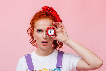 Blue-eyed woman with red hair bandage covers her eyes with small alarm clock