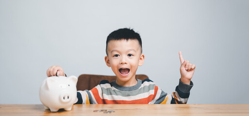 Little Asian boy saving money in piggy bank, learning about saving thinking about something, Kid save money for future education. Money, finances, insurance and people concept