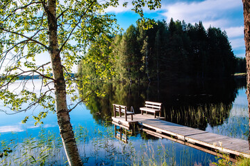 Wooden pier with bench for rest on a blue lake in Finland