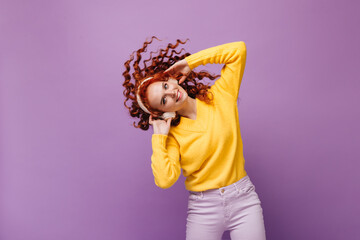 Lovely girl in cashmere sweater listens to music on headphones and plays hair on lilac background