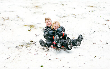 Two boys sharing a toboggan speeding down hill having a great time in the snow