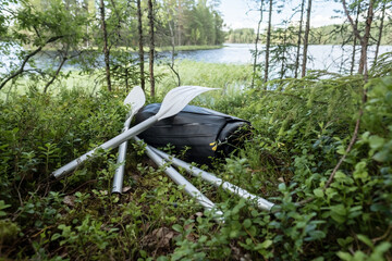 New rubber inflatable boat and oars lie in the grass, on the shore of the lake. Preparing for a boat trip or fishing. Active lifestyle.