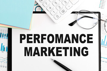 Text Perfomance Marketing on clipboard, pen, glasses, calculator, sticker, graphs. Business concept. Flat lay.