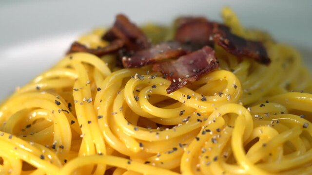 Spaghetti carbonara, a traditional pasta dish of Italian culture made with fresh egg yolk, original grated pecorino romano, crispy bacon, and black pepper.