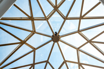 Clear blue sky bottom view through stylish glass ceiling made of large geometric pieces and golden frame in theater hallway