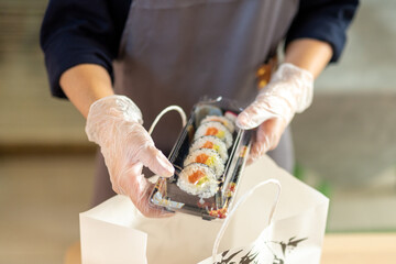 hand of a waitress filling take away box of sashimi and sushi, alternative activities of catering...