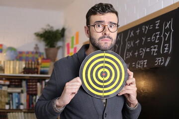 Stressed out teacher holding bullseye target in classroom