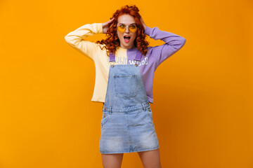 Young girl in sundress and sweatshirt ruffles her curly hair against orange background