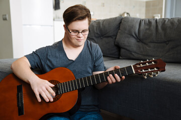 Young man with down syndrome playing guitar while sitting on floor