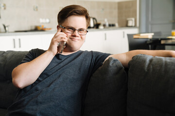 Young man with down syndrome talking on cellphone while sitting at home