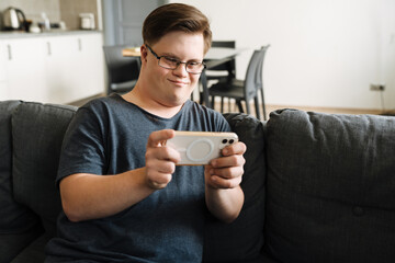 Young man with down syndrome using cellphone while sitting on couch