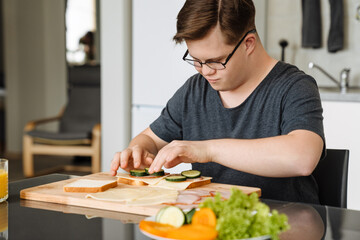 Young man with down syndrome making sandwiches in kitchen at home