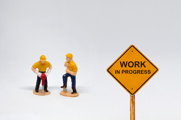 Small figure workers on white background with message Work In Progress 