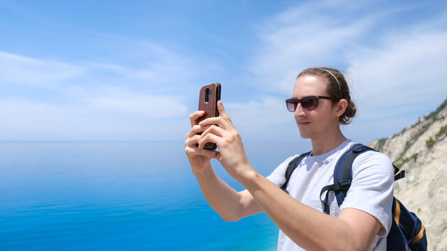 Young man taking pictures of beautiful beach with smartphone