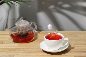 ref fruit tea on wooden table. sugar cube falling in cup. splash of tea. tea pot with fruit tea