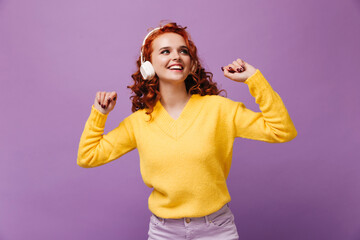 Woman with red curls dancing, listening to music in white headphones