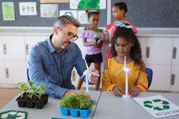 Caucasian male teacher holding windmill model teaching a girl during environment class at school