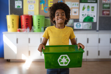 Portrait of african american boy holding tray filled with recyclable plastic items at school