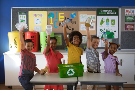 Portrait of group of diverse students smiling while holding recyclable plastic items at school