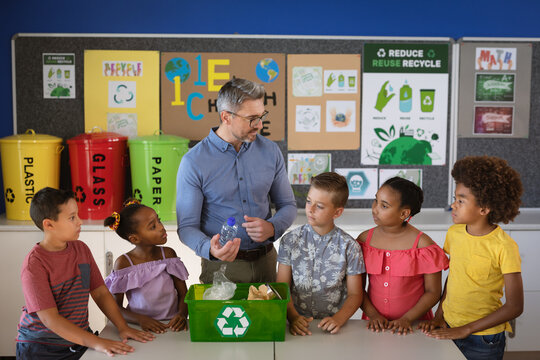 Caucasian male teacher teaching group of diverse students to recycle plastic items at school