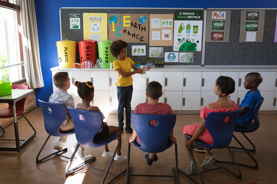 African american boy showing how to recycle plastic items to other students in class at school - Powered by Adobe