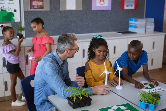 Caucasian male teacher holding windmill model teaching boy and girl in environment class at school