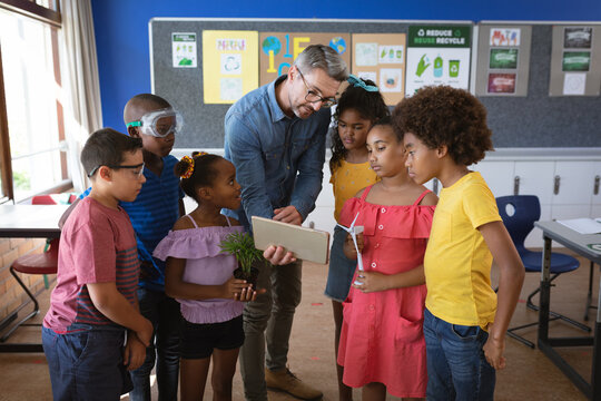 Caucasian male teacher with digital tablet teaching group of diverse students in environment class
