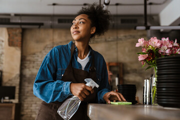 Black waitress wearing apron cleaning table while working in cafe