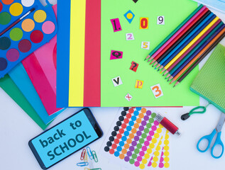 Obraz premium Above view of accessories for back to school, pencils, notebooks, scissors, stationery - education concept - message on mobile phone