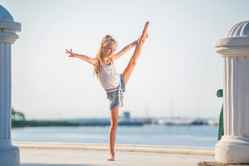 Gymnast teenage girl posing on embankment against background of the sea and sky