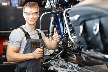 Fototapeta na wymiar Motorcycle repair technician holds thumbs up while standing in workshop