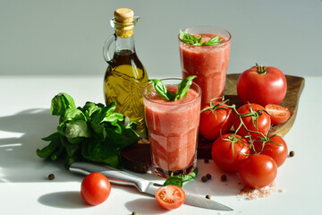 Two glasses of fresh organic tomato juice decorated with raw tomatoes and green leaves of basil on...