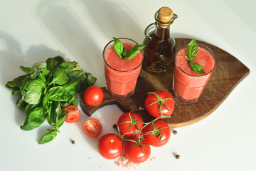 Two glasses of fresh organic tomato juice decorated with raw tomatoes and green leaves of basil on light background.Healthy diet nutrition concept.