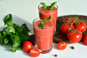 Two glasses of fresh organic tomato juice decorated with raw tomatoes and green leaves of basil on...