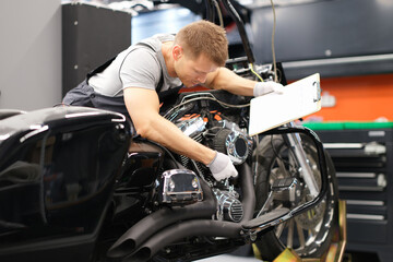 Male mechanic diagnoses parts on motorcycle at service center