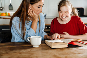 White woman helping her daughter with down syndrome reading book