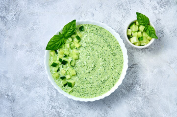 Cucumber Gazpacho - cold summer soup with basil in white bowl on light background. Top view Flat lay.
