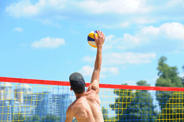 Beach volleyball. Male volley player hitting ball over the net attacking