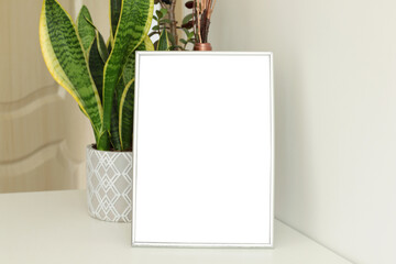 blank vertical frame on white table and plants on the background