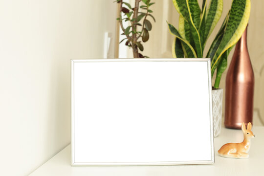 empty photo frame on white table with flower pots on background