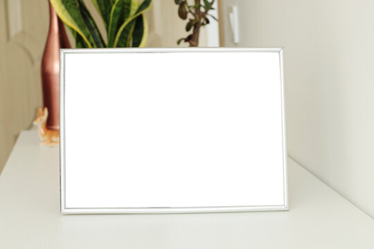 empty horizontal photo frame on white table with flower pots on background