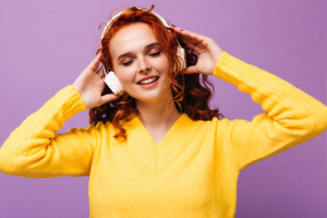 Joyful girl in yellow sweater and headphones listens to songs with smile
